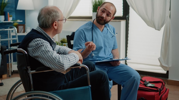 Asystent medyczny konsultujący starca z niepełnosprawnością w domu opieki. emerytowany pacjent na wózku inwalidzkim rozmawia z pielęgniarką w celu sprawdzenia choroby i leczenia w ramach opieki zdrowotnej. niepełnosprawny