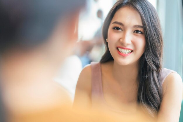 Atrakcyjna azjatycka pozytywna rozmowa o kobiecym szczęściu uśmiechnięta śmiech wesoła rozmowa z przyjacielem w kawiarni restauracji z naturalnym światłem z okna koncepcja swobodnego stylu życia