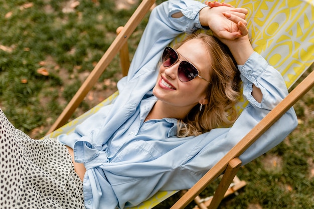 Atrakcyjna blond uśmiechnięta kobieta siedzi w leżaku w letnim stroju