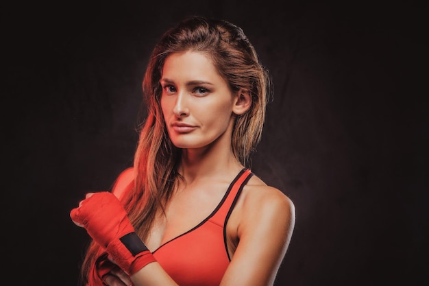 Atrakcyjna brunetka w czerwonych rękawiczkach i sportowym staniku pozuje dla fotografa w studio.