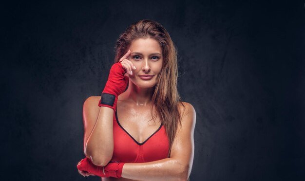 Atrakcyjna brunetka w czerwonych rękawiczkach i sportowym staniku pozuje dla fotografa w studio.