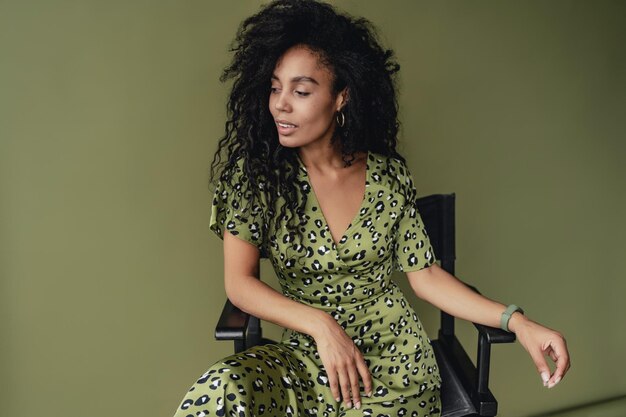 Atrakcyjna czarna afroamerykanka pozuje w stylowej zielonej sukience na zielonym tle