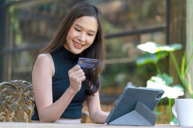 Atrakcyjna dorosła azjatycka kobieta szczęście zakupy online z laptopem ręka trzyma kartę kredytową i smartfon do zakupu produktu z tłem koncepcji pomysłów na biznes kawiarnia restauracja