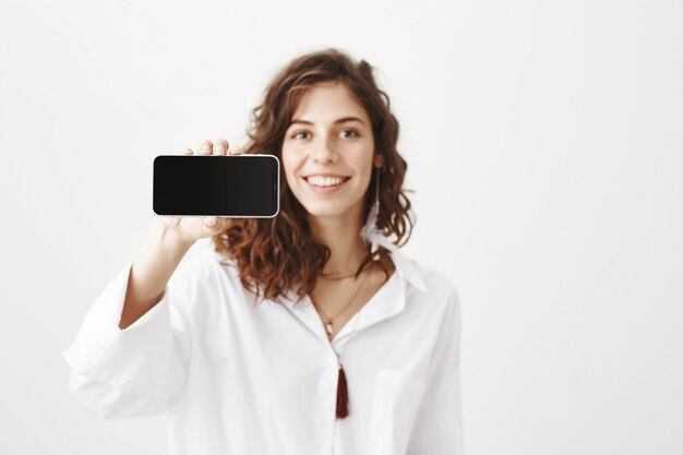 Atrakcyjna kobieta pokazująca wyświetlacz smartfona, reklamująca aplikację