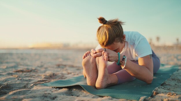 Atrakcyjna kobieta robi ćwiczenia jogi na świeżym powietrzu Nauczyciel jogi ćwiczący na macie rozciągającej ciało podczas porannej jogi na plaży