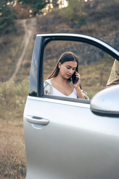 Bezpłatne zdjęcie atrakcyjna kobieta rozmawia przez telefon, stojąc przy samochodzie w przyrodzie