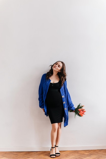 Atrakcyjna Kobieta W Ciąży W Czarnej Sukience I Niebieskim Swetrze Trzyma Bukiet Tulipanów Brunetka Dama Pozuje Na Na Białym Tle