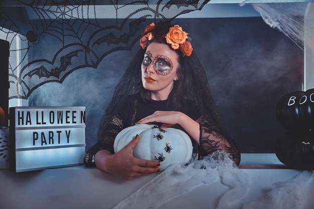 Atrakcyjna kobieta w roli ciemnej martwej panny młodej pozuje fotografowi z dekoracjami na Halloween.