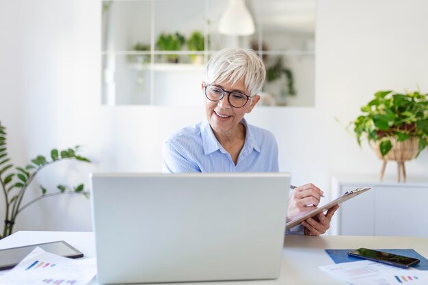Atrakcyjna kobieta w średnim wieku siedząca przed laptopem i prowadząca swoją małą firmę z domu