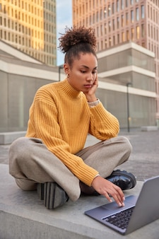 Atrakcyjna kobieta z kręconymi włosami pracuje jako niezależna na laptopie ogląda wideo w czasie wolnym