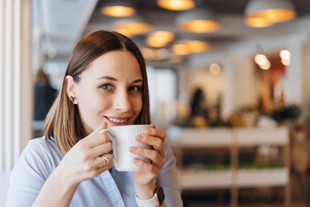 Atrakcyjna kobieta z uroczym uśmiechem, pijąc kawę, relaksując się w przerwie