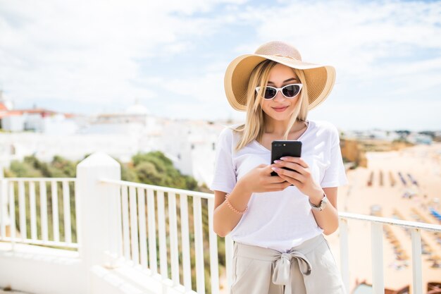 Atrakcyjna młoda blond kobieta pisania na telefon na tarasie z widokiem na plażę