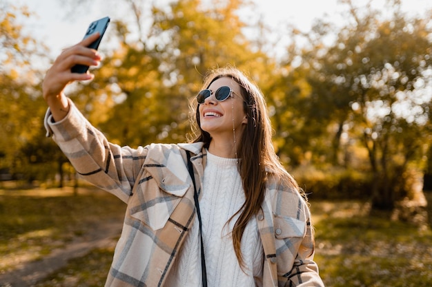 Atrakcyjna młoda kobieta chodząca jesienią ubrana w kurtkę za pomocą telefonu