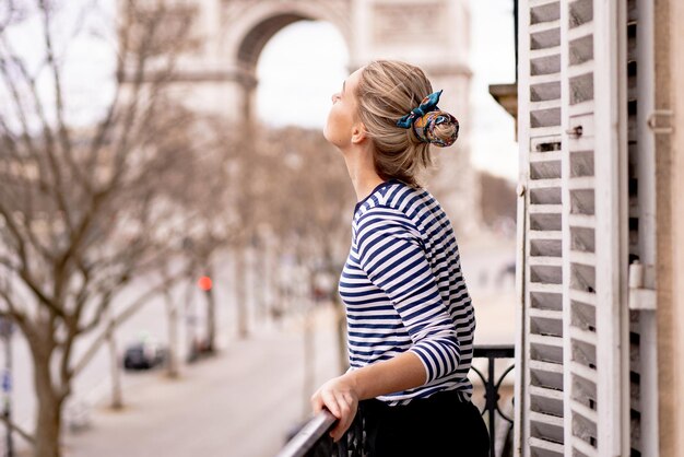 Atrakcyjna młoda kobieta na balkonie rano w mieście Paryż. widok na łuk triumfalny.