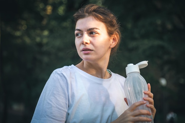 Bezpłatne zdjęcie atrakcyjna młoda kobieta pije wodę po biegu w parku treningu w przyrodzie