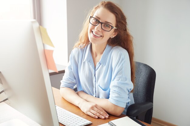 Atrakcyjna młoda kobieta przedsiębiorca z rudymi włosami i okularami, patrząc i uśmiechnięty