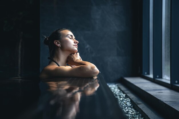 Atrakcyjna młoda kobieta w czarnym stroju kąpielowym relaksuje się w basenie