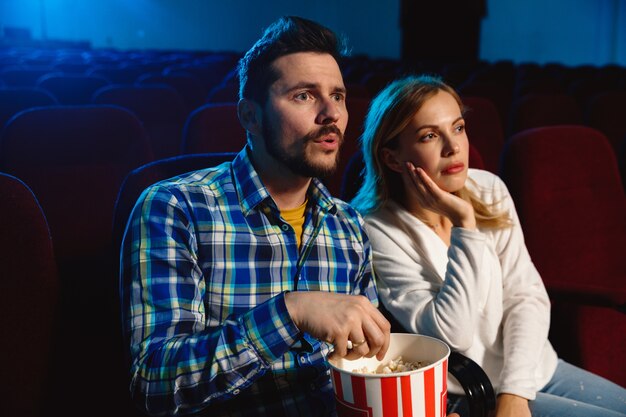 Atrakcyjna młoda para kaukaski ogląda film w kinie, domu lub kinie. Wyglądaj wyraziście, zdziwiony i emocjonalny. Siedzenie samotnie i dobra zabawa. Relacja, miłość, rodzina, weekend.