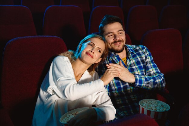 Atrakcyjna młoda para kaukaski ogląda film w kinie, domu lub kinie. Wyglądaj wyraziście, zdziwiony i emocjonalny. Siedzenie samotnie i dobra zabawa. Relacja, miłość, rodzina, weekend.