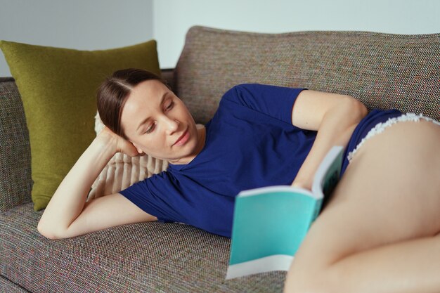 Atrakcyjna pozytywna kobieta czyta książkę relaksuje na kanapie