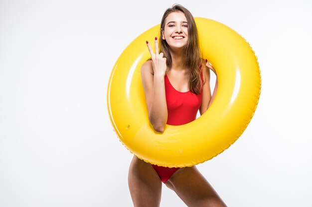 Atrakcyjna seksowna piękna kobieta w czerwonym kostiumie kąpielowym posiada okrągły żółty materac dmuchany na białym tle