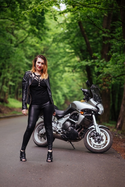 Atrakcyjna sexy dziewczyna ubrana w skórę pozuje w pobliżu motocyklu sportowego na zewnątrz