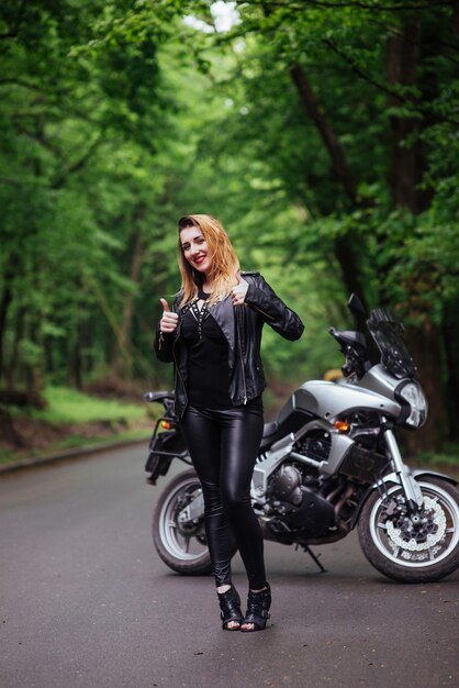 Atrakcyjna sexy dziewczyna ubrana w skórę pozuje w pobliżu motocyklu sportowego na zewnątrz