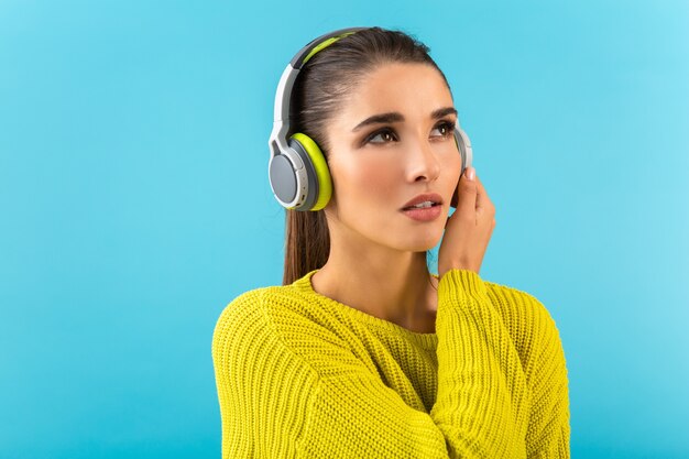 Atrakcyjna stylowa młoda kobieta słucha muzyki w słuchawkach bezprzewodowych szczęśliwa sobie żółty sweter z dzianiny kolorowy styl moda pozowanie