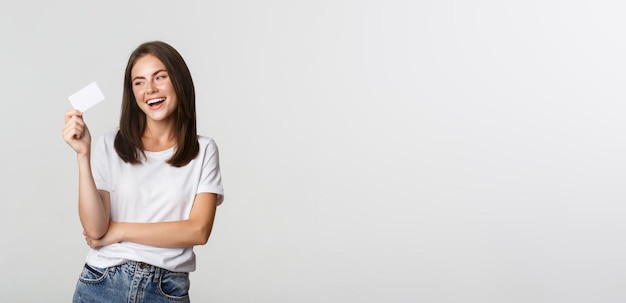 Atrakcyjna szczęśliwa brunetka dziewczyna śmiejąca się i trzymająca białe tło karty kredytowej