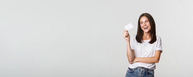 Atrakcyjna, szczęśliwa brunetka śmiejąca się i trzymająca kartę kredytową na białym tle