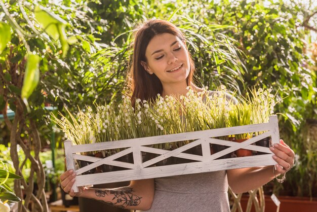 Bezpłatne zdjęcie atrakcyjna szczęśliwa kobieta trzyma drewnianą półkę z roślinami