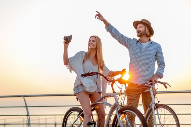 Atrakcyjna szczęśliwa para podróżująca latem na rowerach, mężczyzna i kobieta o blond włosach moda w stylu boho hipster, wspólna zabawa, robienie zdjęć zwiedzanie