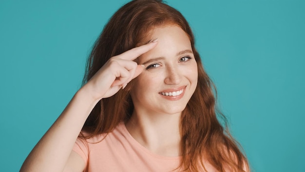 Atrakcyjna uśmiechnięta rudowłosa dziewczyna szczęśliwie pokazująca do zobaczenia później gest przed kamerą na kolorowym tle