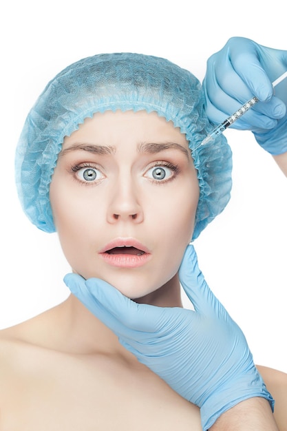 Atrakcyjna zaskoczona i przestraszona kobieta w chirurgii plastycznej ze strzykawką w twarzy na białym tle