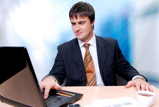 Atrakcyjny biznesmen siedział przy biurku i pracy na laptopie