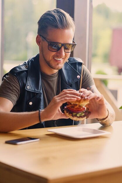 Atrakcyjny hipster ubrany w skórzaną kurtkę jedzący wegańskiego burgera.