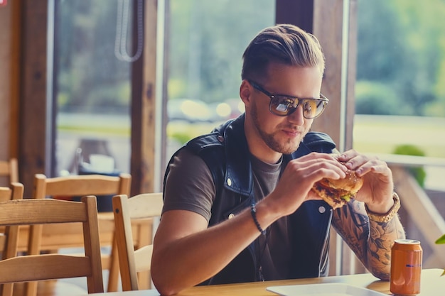 Atrakcyjny hipster ubrany w skórzaną kurtkę jedzący wegańskiego burgera.