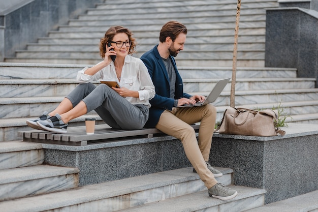Atrakcyjny mężczyzna i kobieta siedzący na schodach w centrum miasta, pracujący razem na laptopie