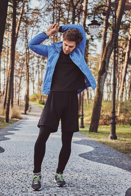 Atrakcyjny sportowy student robi rozciąganie w parku w godzinach porannych.