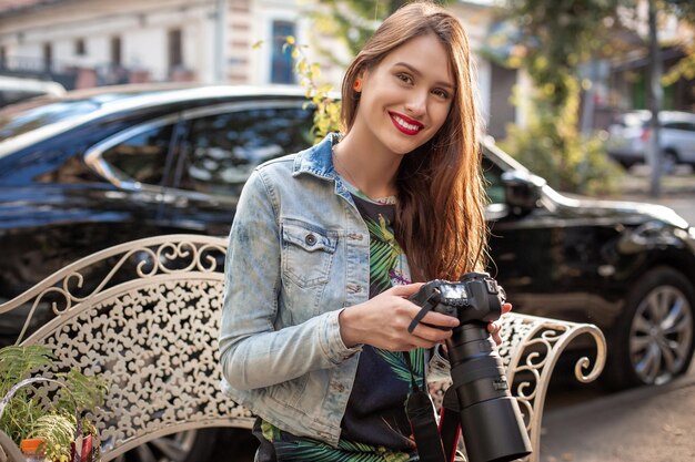 Atrakcyjny turystyczny fotograf kobieta z aparatem, odkryty przy ulicy miasta. Wspaniała szczęśliwa kaukaska kobieta w swobodnych modnych ubraniach