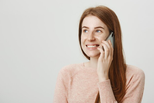 Attactive uśmiechnięta ruda kobieta rozmawia przez telefon komórkowy