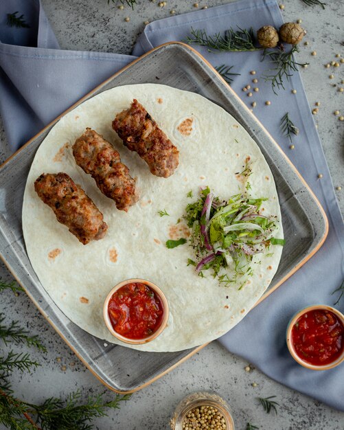 Azerbaijani lule kebab, grill z zieloną sałatą i czerwonym sosem w lawaszu.