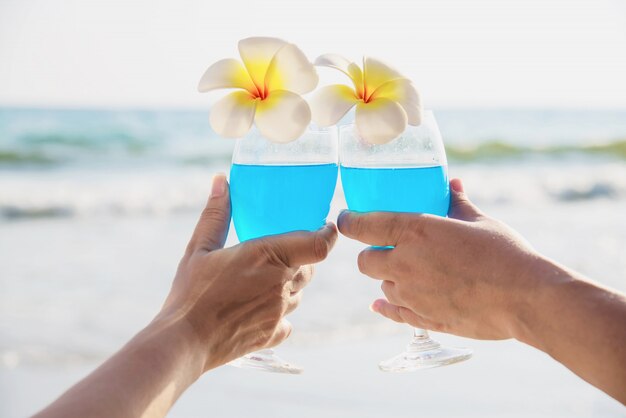 Azjatycka Ccouple mienia koktajlu szkła dekoracja z plumeria kwiatem z falową denną plażą - szczęśliwy relaksuje świętowania wakacje w dennym natury pojęciu
