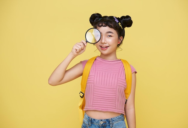 Bezpłatne zdjęcie azjatycka dziewczynka studentka trzymająca szkło powiększające i patrząca na kamerę z ciekawym wyrazem twarzy