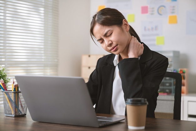 Azjatycka kobieta biznesu ma ból karku, ponieważ korzysta z komputera i pracuje przez długi czas w biurze.
