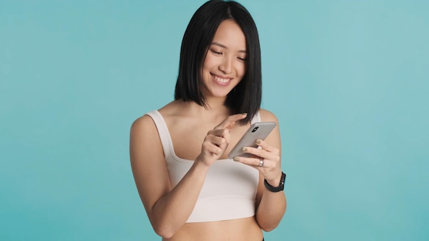 Azjatycka kobieta przeglądająca sieć społecznościową na kolorowym tle Azjatycka kobieta wyglądająca na szczęśliwą używającą smartfona na białym tle Nowoczesna technologia