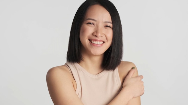 Azjatycka kobieta szczerze uśmiecha się do kamery, wyglądając tak szczęśliwie na białym tle Wesoła Azjatycka dziewczyna