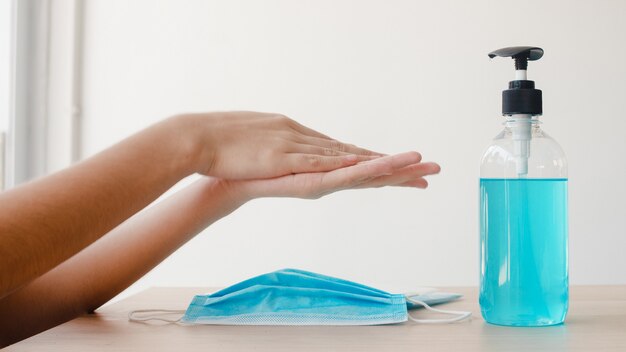 Azjatycka kobieta używa alkoholowego gel dezynfekci ręki myj rękę przed odzieży maską dla ochrony koronawirusa. Kobieta popycha alkohol do czyszczenia w celu zachowania higieny, gdy dystans społeczny zostaje w domu i poddaje się kwarantannie.