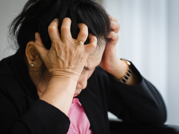 Azjatycka kobieta w średnim wieku, starsza kobieta, odczuwa ból i cierpi na nagły ból głowy oraz atak udaru mózgu i trzyma się wokół głowy ze zestresowaną twarzą. pojęcie problemu mózgu i głowy.