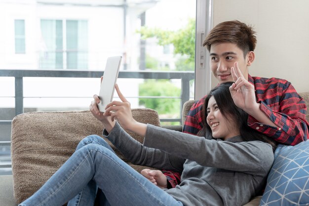 Azjatycka młoda kobieta i przystojny mężczyzna obsiadanie na kanapie używać urządzenie
